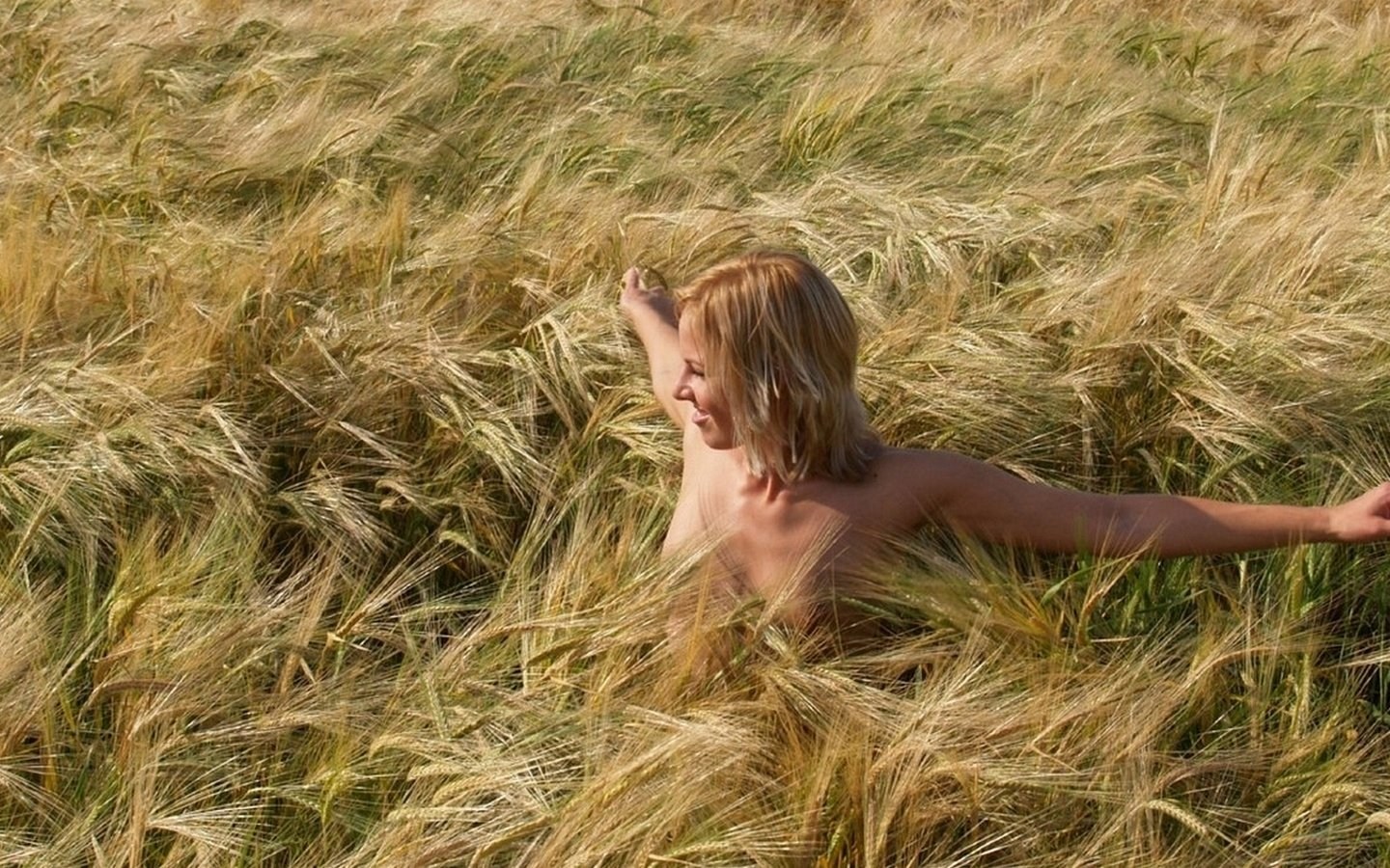Загорелая девка позирует голышом в поле с соломой